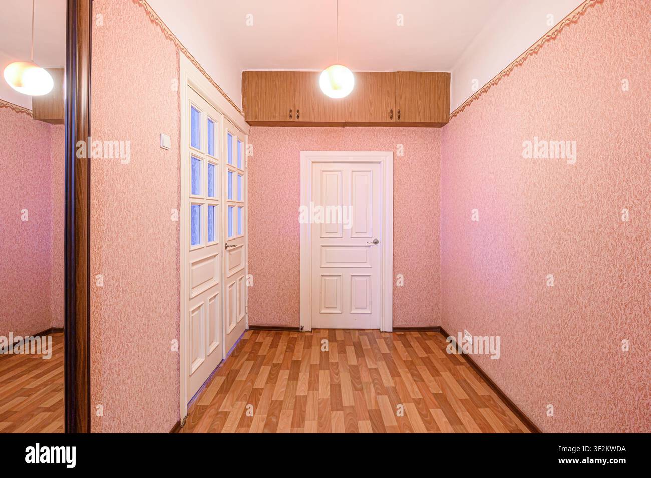 stanza vintage con carta da parati rosa, pavimento in legno, porte bianche, armadi sospesi e una lampada a sospensione sferica Foto Stock