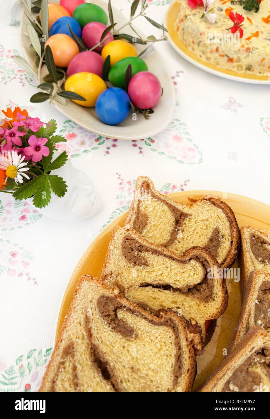 Fette di pane dolce tradizionale rumeno Cozonac con ripieno di cacao e noci, su una tavola festosa con uova di Pasqua dipinte a colori vivaci. Foto Stock
