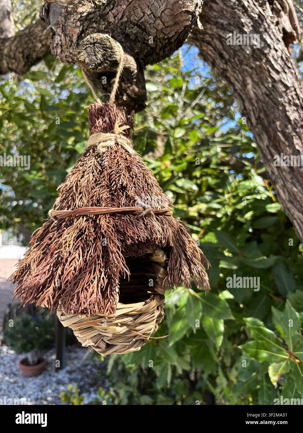 Rifugio per nidi d'uccello in fibre naturali fatto a mano, appeso in un giardino verde. Casetta per uccelli rustica ed ecologica per la fauna del cortile e gli uccelli piccoli. Foto Stock