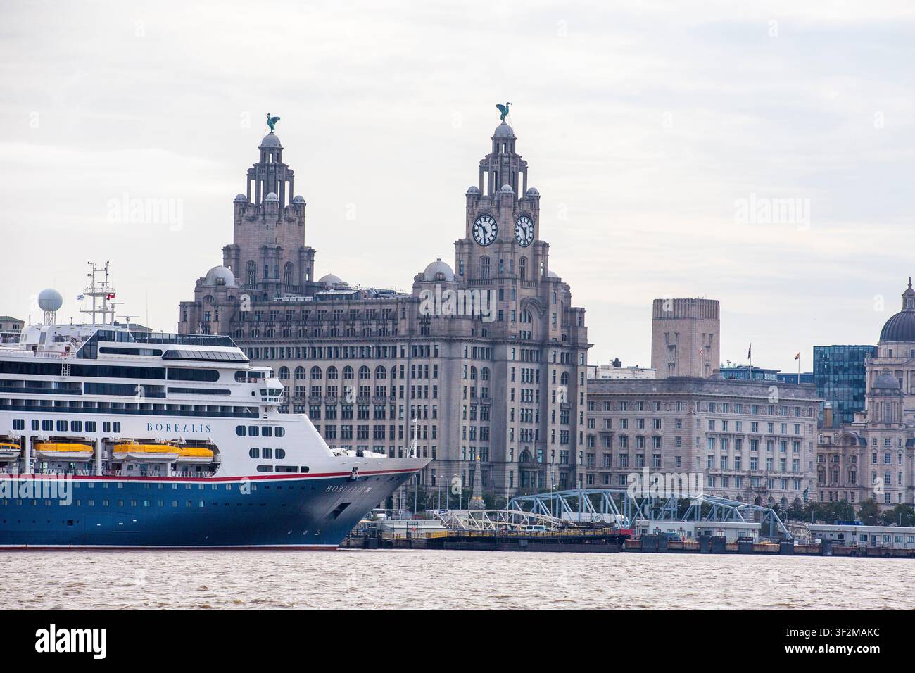 Grandi argini del porto di Liverpool con le iconiche torri del Liver Building. Una grande nave da crociera è ormeggiata al molo, riflettendosi nelle acque calme. L'architettura storica domina Foto Stock