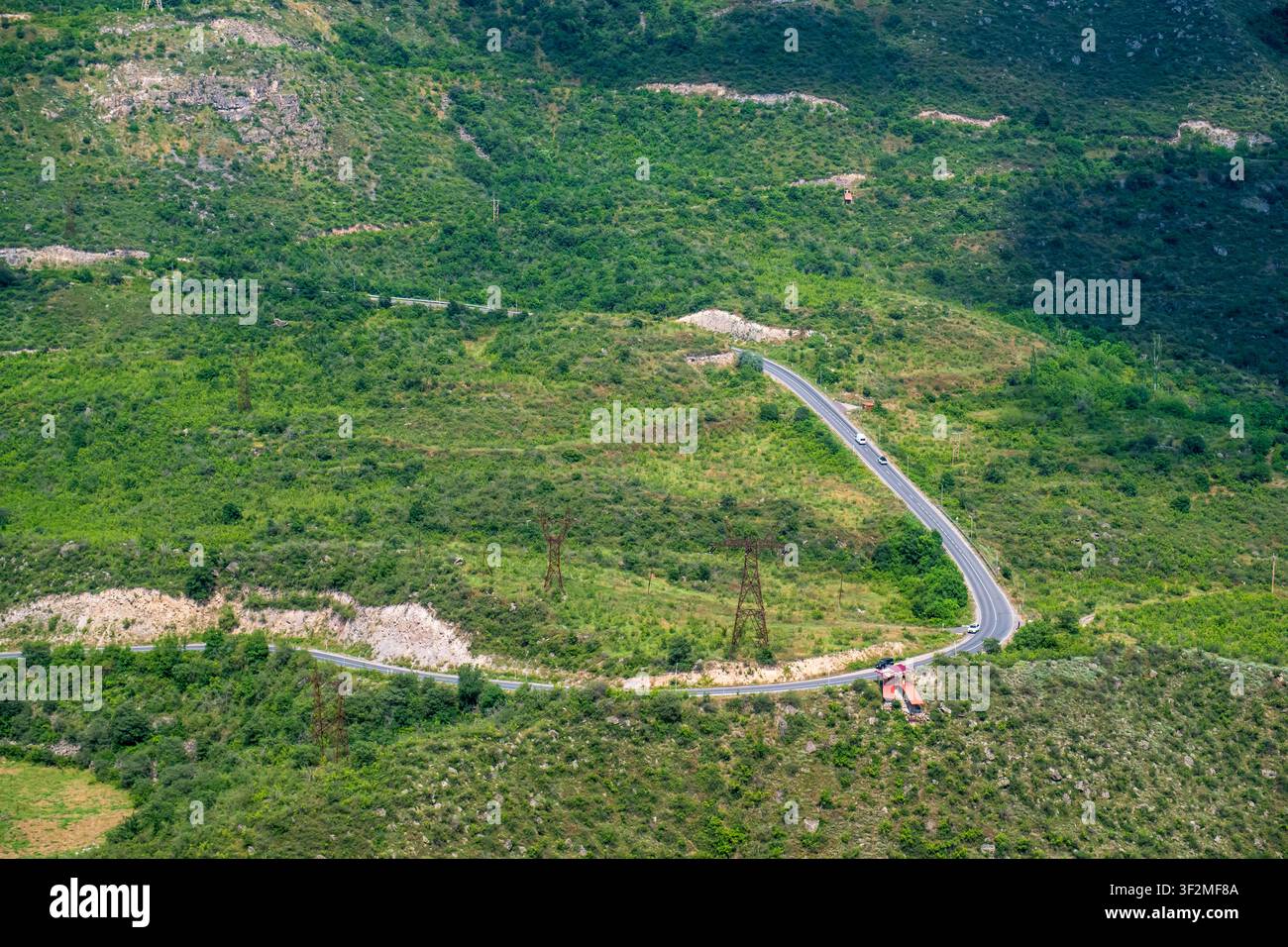 Strada tortuosa si snoda attraverso colline verdi e rigogliose sotto un cielo blu brillante Foto Stock