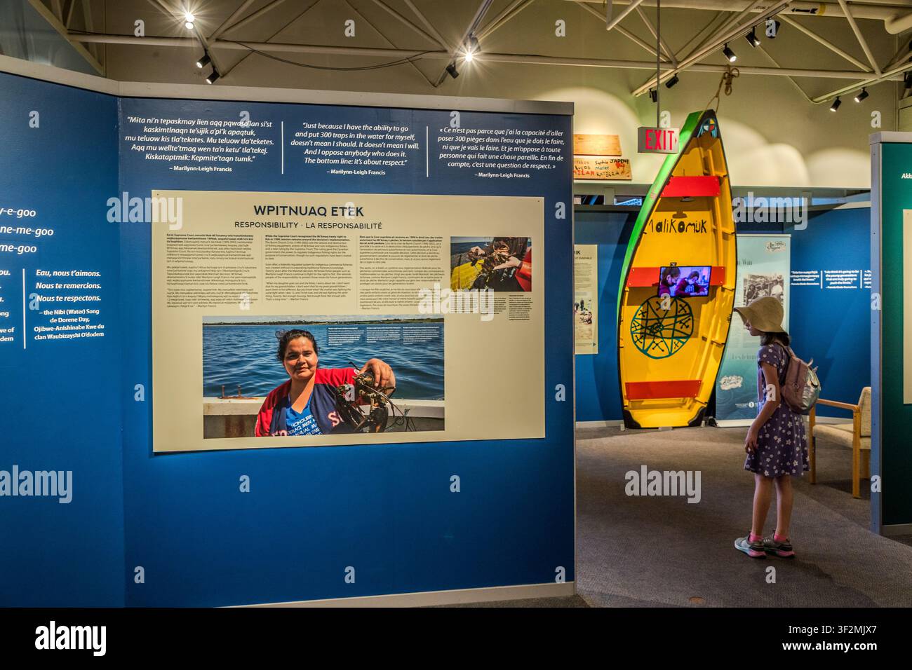 Ritratto e pannello di citazione con la pescatrice di aragosta Marilynn-Leigh Francis nella sezione ‚Wpitnuaq Etek – Responsabilità‘ della mostra mi’kmaq ‚Ta’n me’j Tel-keknuo’ltiek‘ al Maritime Museum of the Atlantic di Halifax, Nuova Scozia, Canada. sullo sfondo c’è una barca dipinta di giallo con l’iscrizione ‚Malikonuk‘. Halifax, Nuova Scozia, Canada Foto Stock