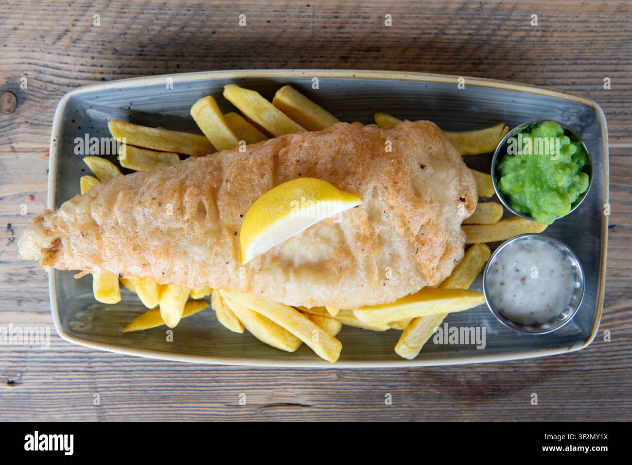 Deliziosi pesce e patatine fritte croccanti serviti con salsa tartara e piselli in purea Foto Stock