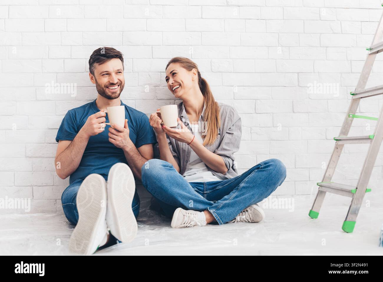 Giovane coppia sorridente bere tè e caffè in appartamento nuovo Foto Stock