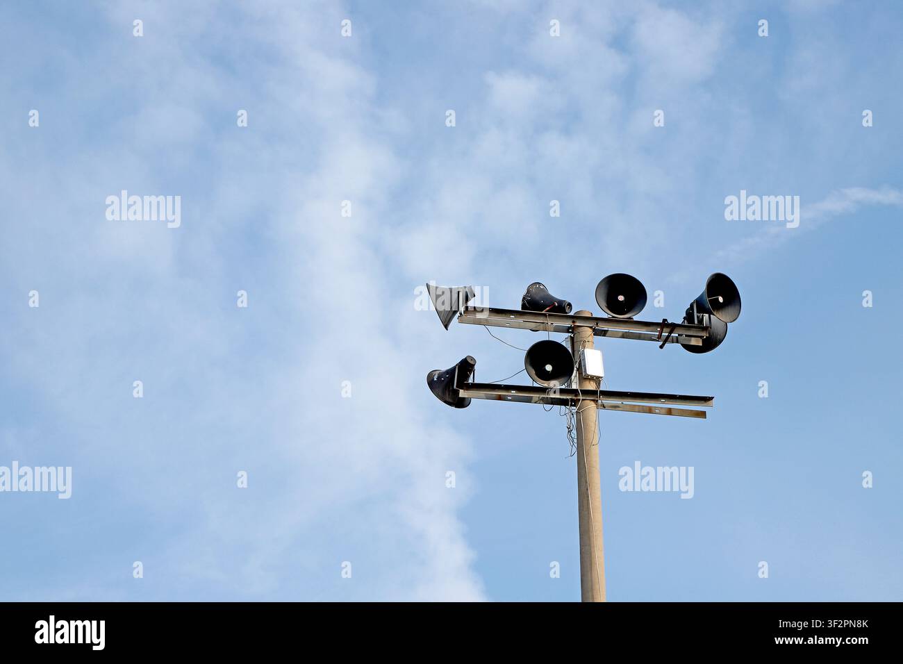 Più altoparlanti neri per trasmissioni sono montati su un palo di servizio in legno contro un cielo azzurro con nuvole bianche. Questi simboli sonori iconici della campagna C Foto Stock