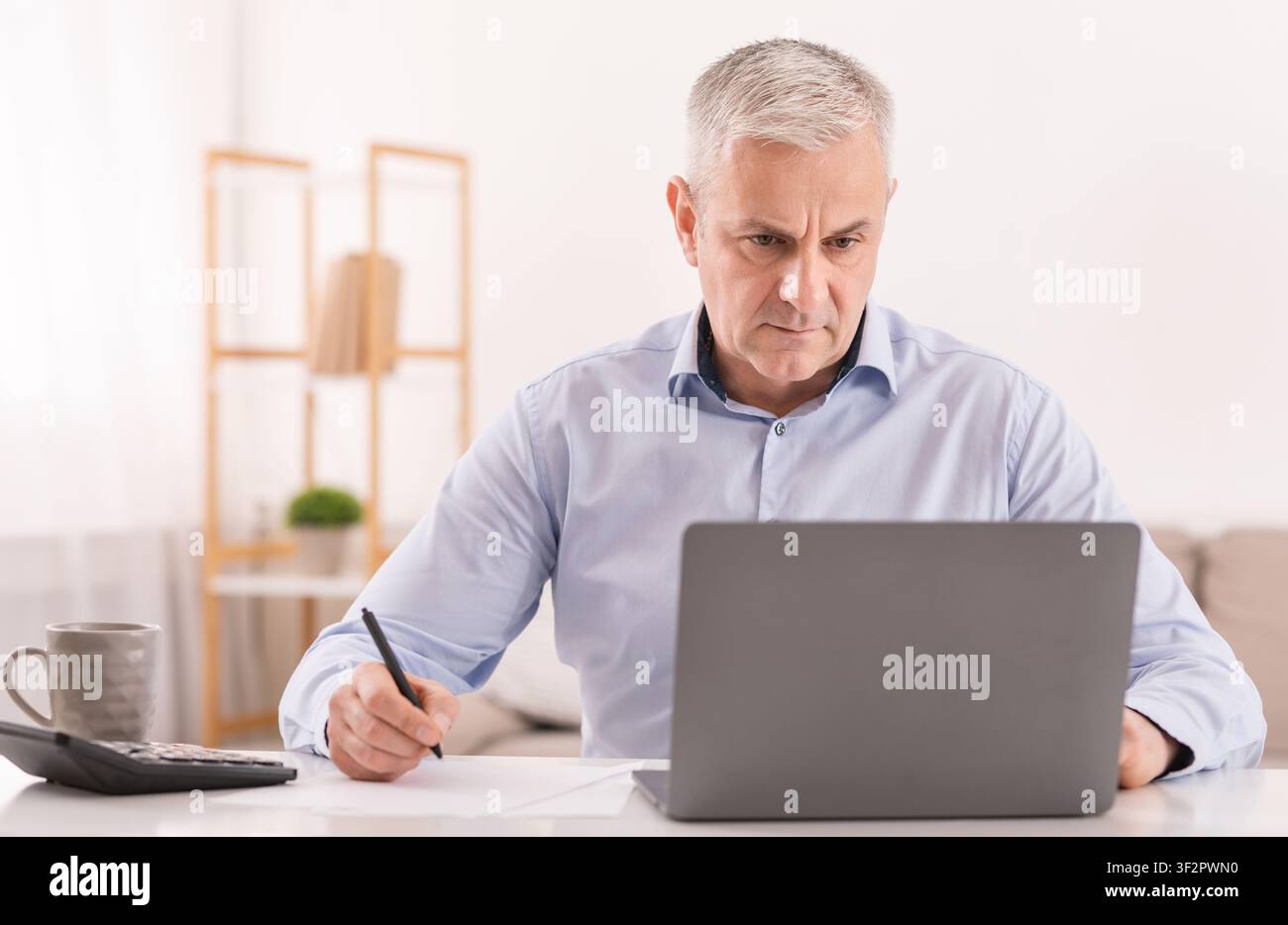 Uomo anziano che usa il laptop in ufficio e scrive le note Foto Stock