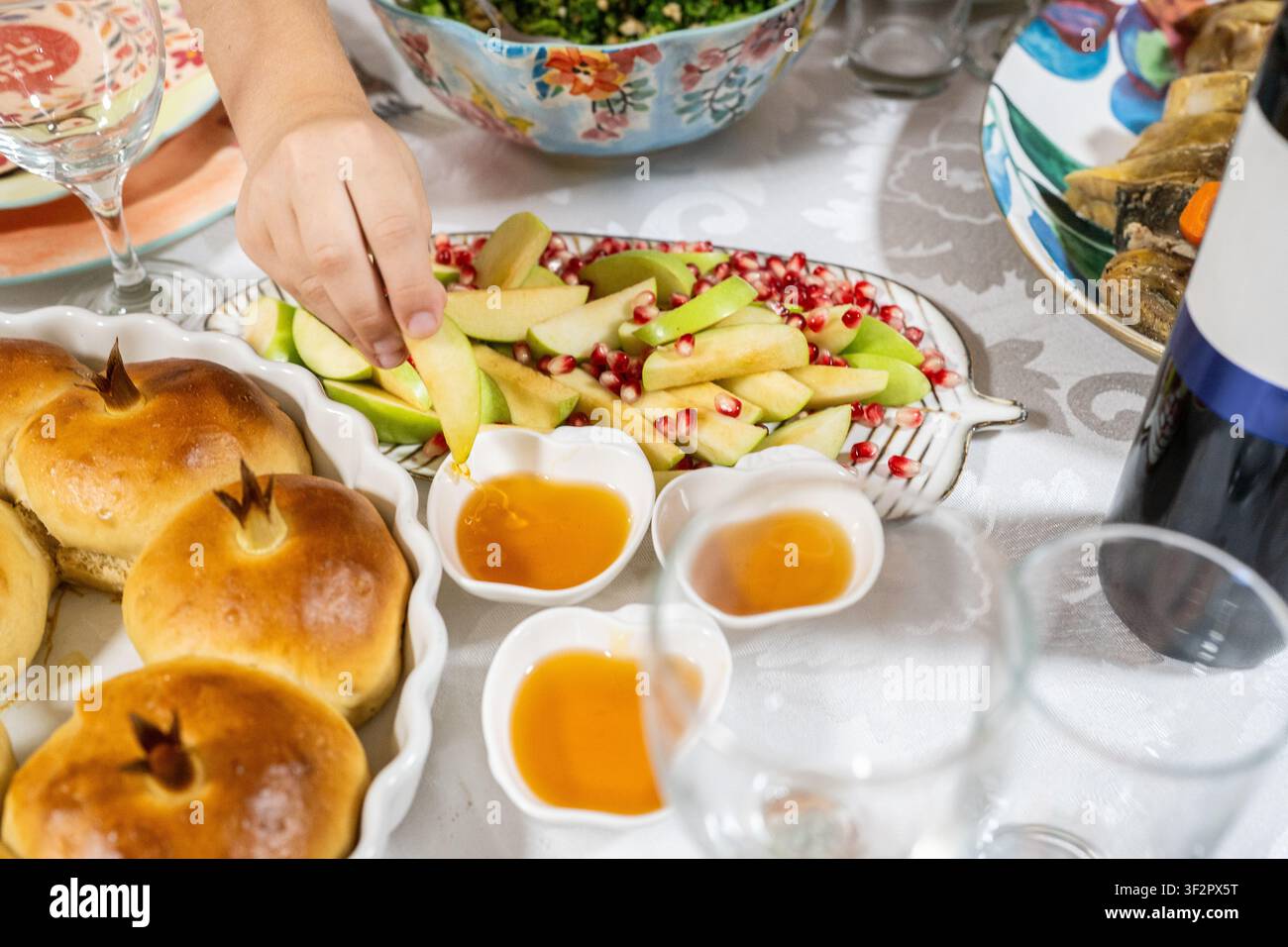 Le persone si riuniscono per celebrare Rosh Hashanah. Un tavolo è apparecchiato con mele, miele e pane challah rotondo. Le mani si protendono verso i cibi dolci che simboleggiano i desideri per un buon anno. Foto Stock