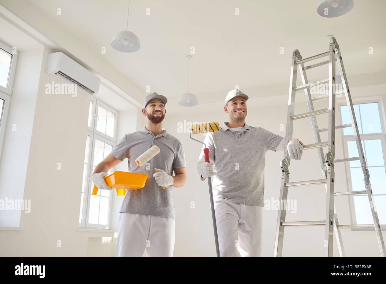 Pittori di case in piedi in una stanza vuota vicino alla scala che si prepara a dipingere il muro di un nuovo appartamento. Foto Stock