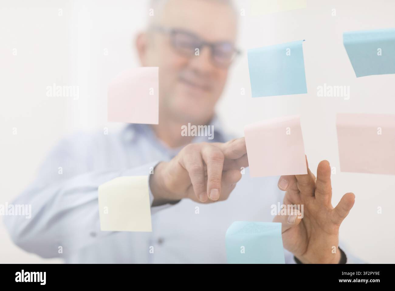 Responsabile anziani che mette le note adesive sulla finestra Foto Stock