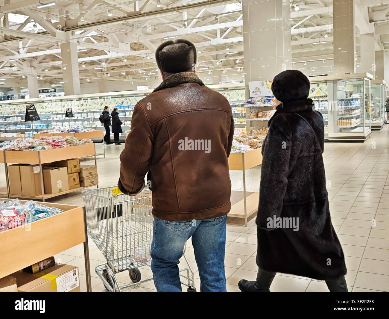 Kirov, Russia - 08 febbraio 2026: I clienti camminano attraverso un negozio di alimentari, spingendo un carrello mentre scelgono prodotti alimentari dagli scaffali in un corridoio pieno di Foto Stock