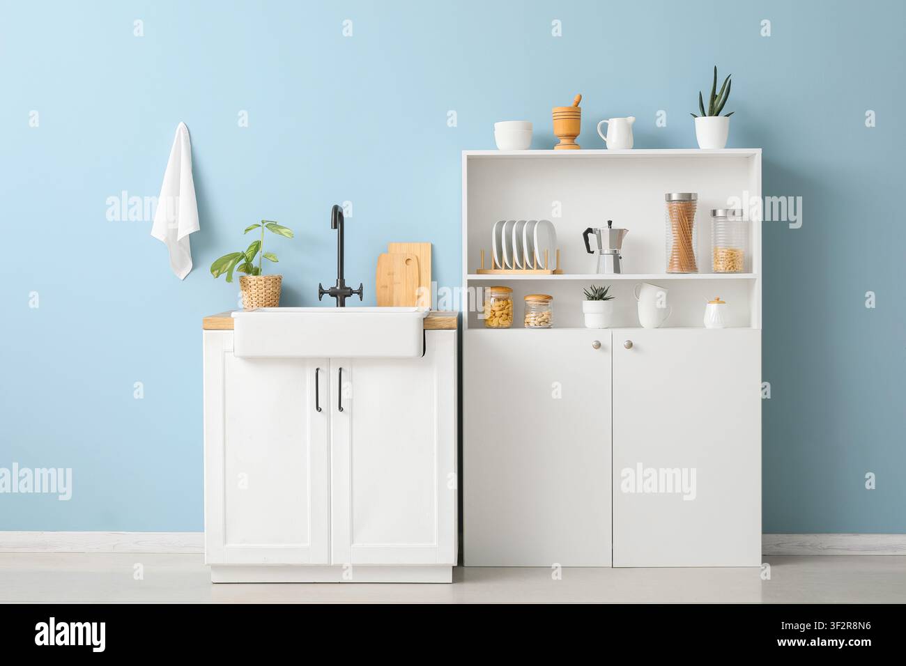 Interno di cucina moderno con armadi bianchi, lavello stile country, rubinetto nero e scaffali aperti contro un muro azzurro Foto Stock