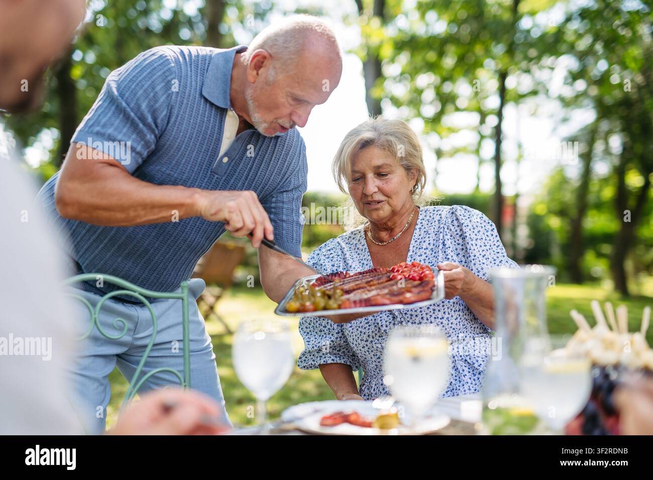 La famiglia condivide il cibo durante la festa al grill in giardino. Foto Stock