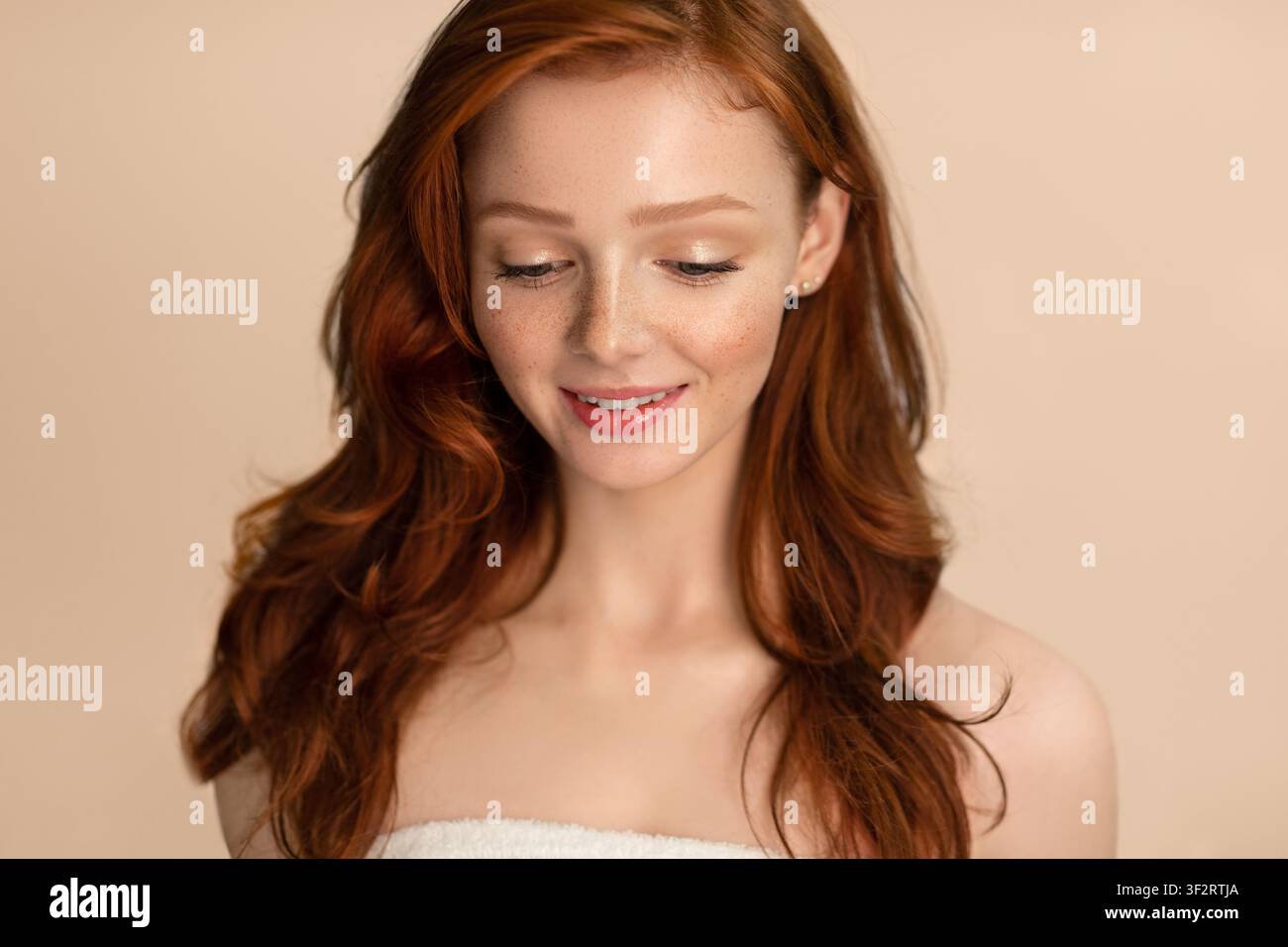 Giovane donna in piedi avvolta in un asciugamano che guarda in basso, sfondo beige Foto Stock
