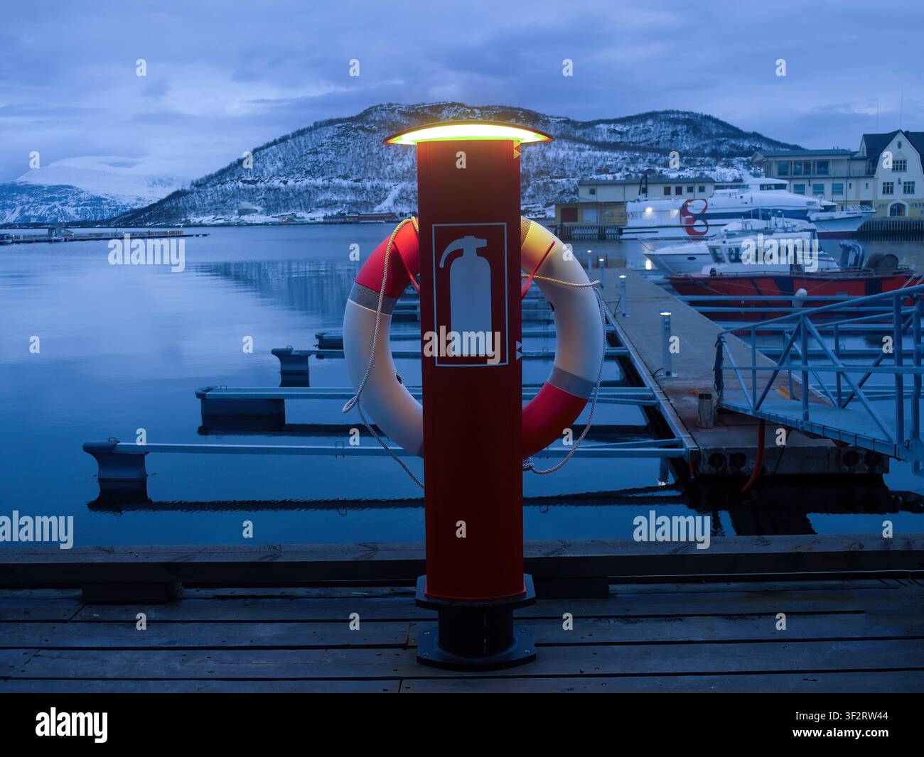 Una foto atmosferica di un palo di sicurezza rosso sul molo, con un anello di salvataggio e un simbolo di estintore illuminato da una luce calda incorporata. Il primo piano Foto Stock