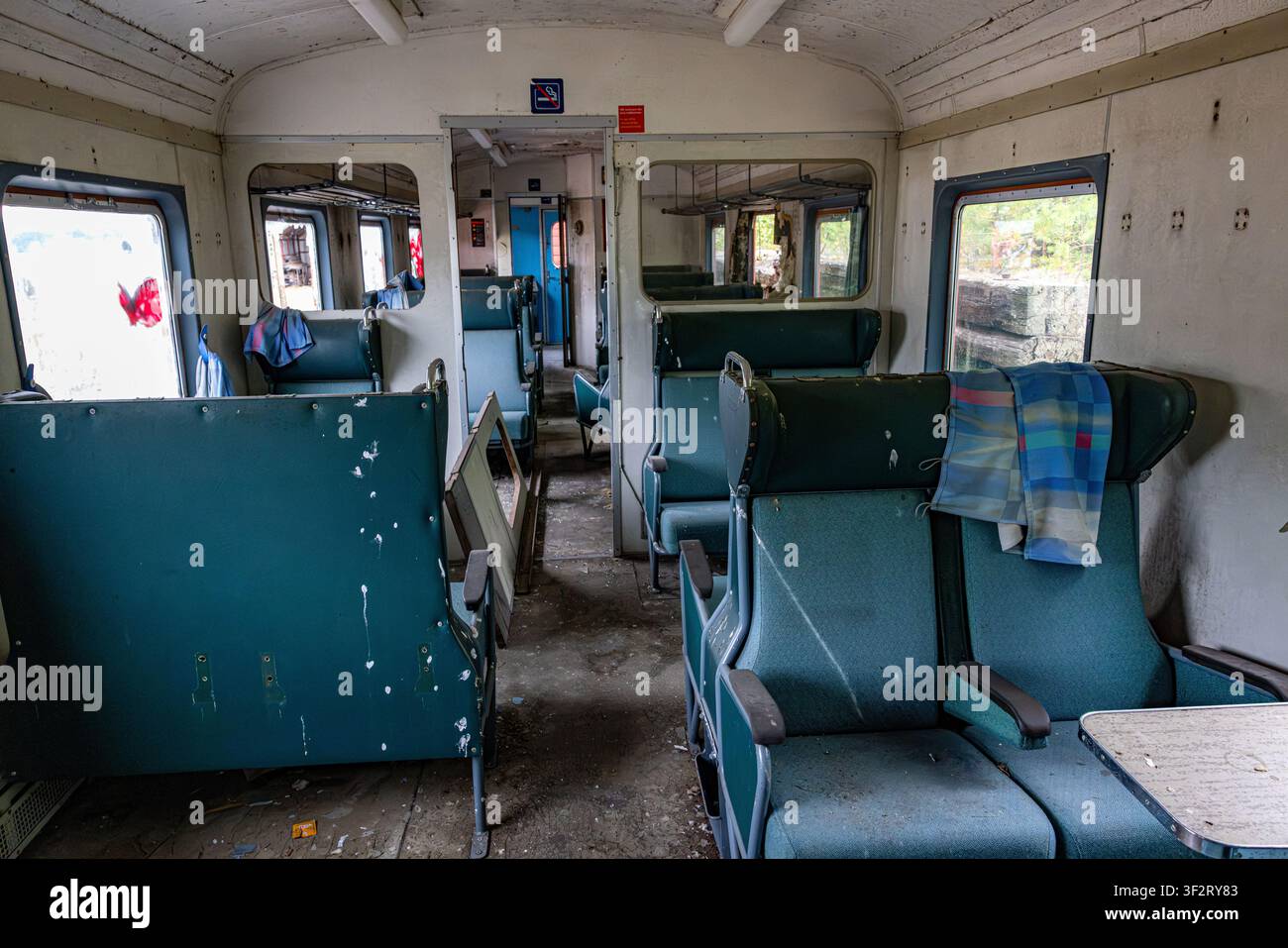 Stazione di Tinnoset, Norvegia. Un vagone del treno vuoto mostra sedili turchesi consumati e sbiaditi. Pavimento polveroso, pareti crepate e specchi sbiaditi riflettono il degrado. La luce del sole filtra Foto Stock