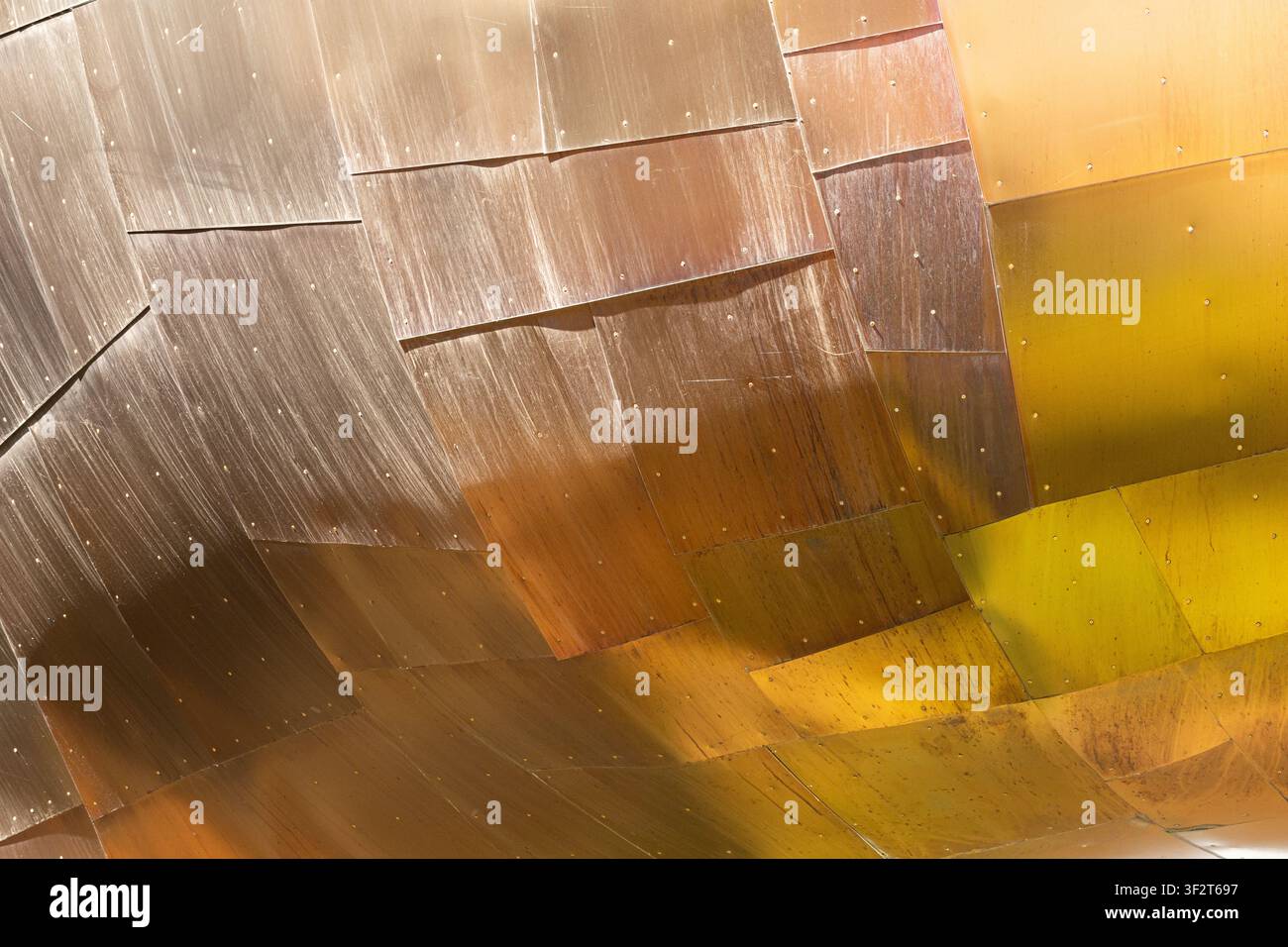 Primo piano astratto di pannelli architettonici metallici curvi con riflessi caldi e motivi geometrici sulla superficie. Foto Stock