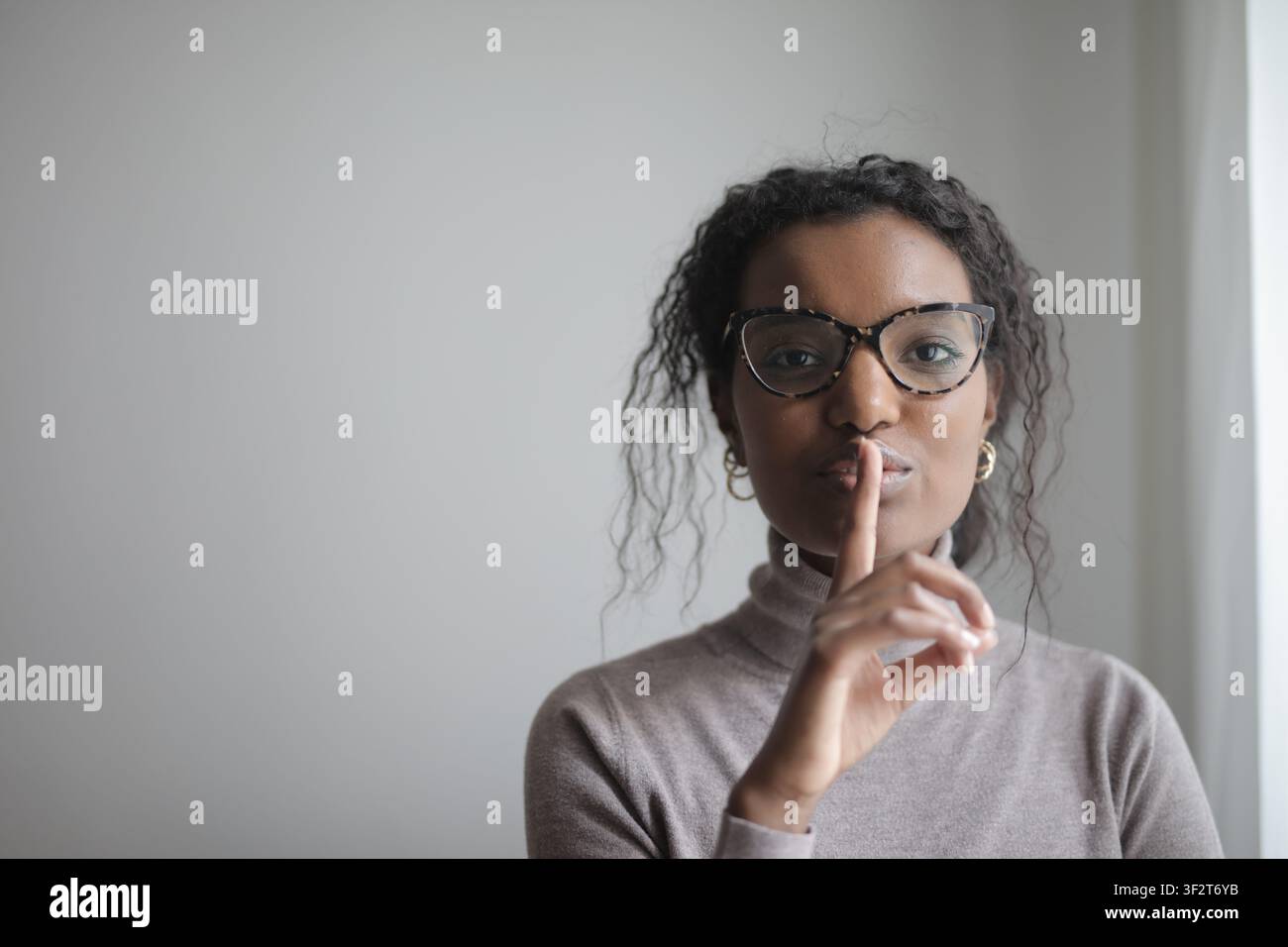 Donna nera con un dito sulle labbra che chiede silenzio Foto Stock
