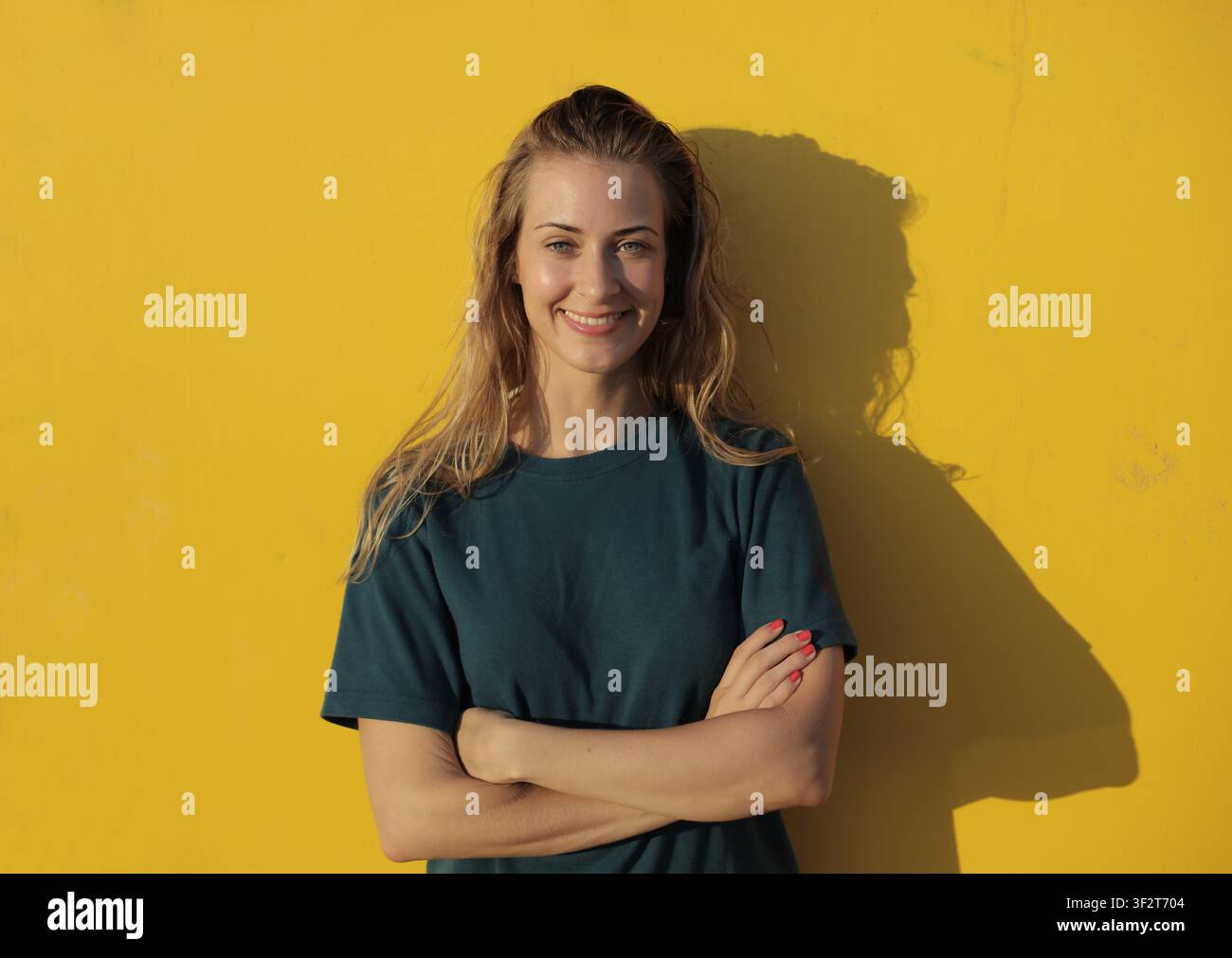 Giovane donna felice che sorride davanti a un muro giallo brillante Foto Stock