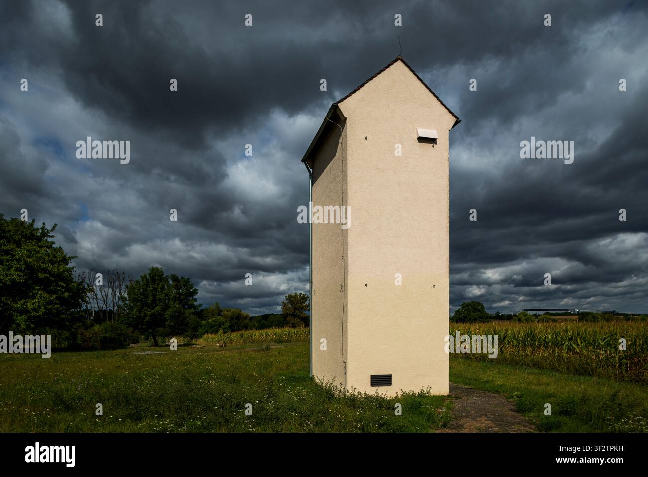 Piccola stazione elettrica rurale per trasformatori sotto drammatiche nuvole di tempesta nella campagna tedesca, circondata da prati Foto Stock