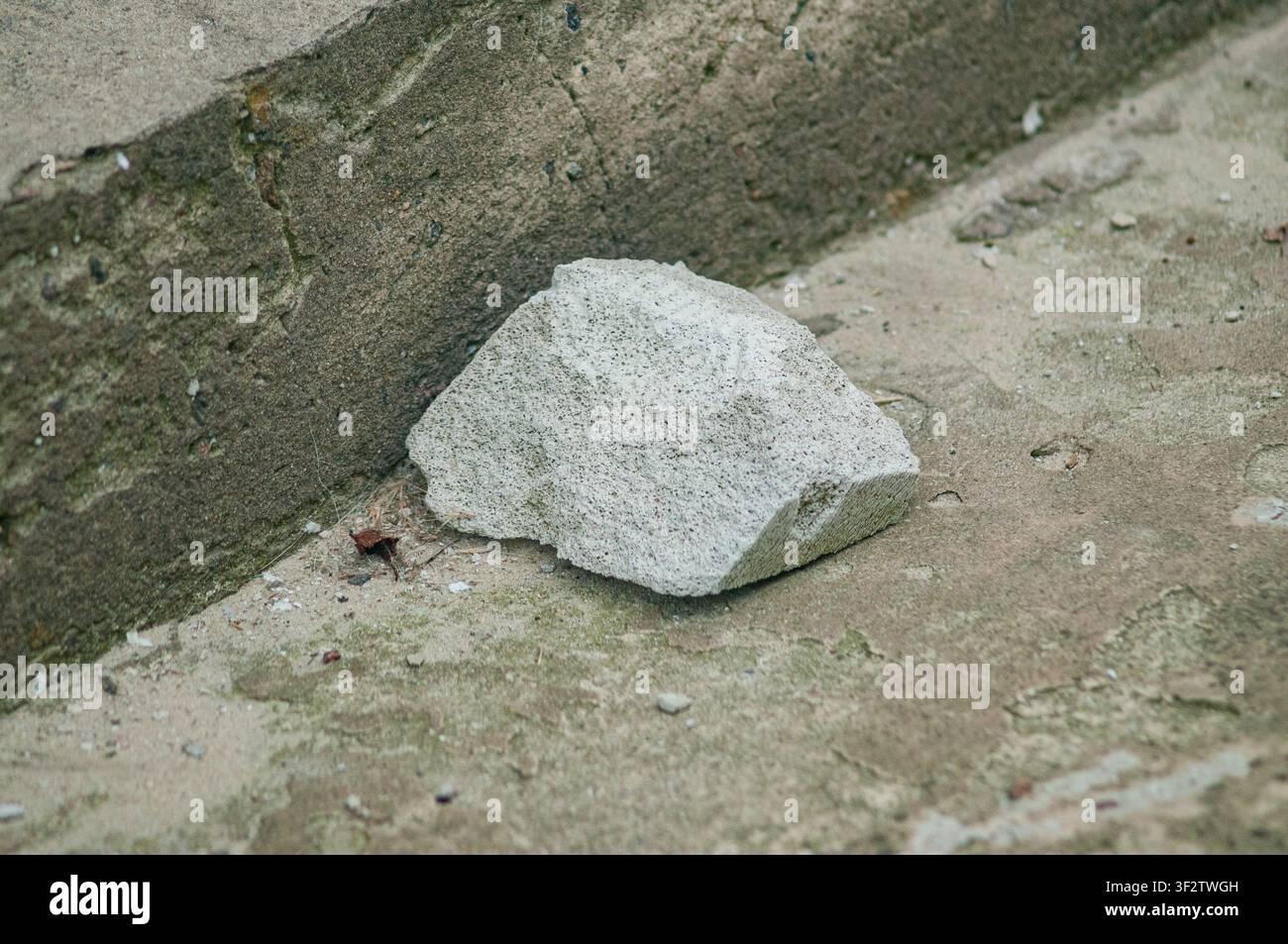 Un primo piano di una singola pietra grigio chiaro e porosa appoggiata su un terreno di cemento ruvido e scolorito in un ambiente all'aperto. Foto Stock