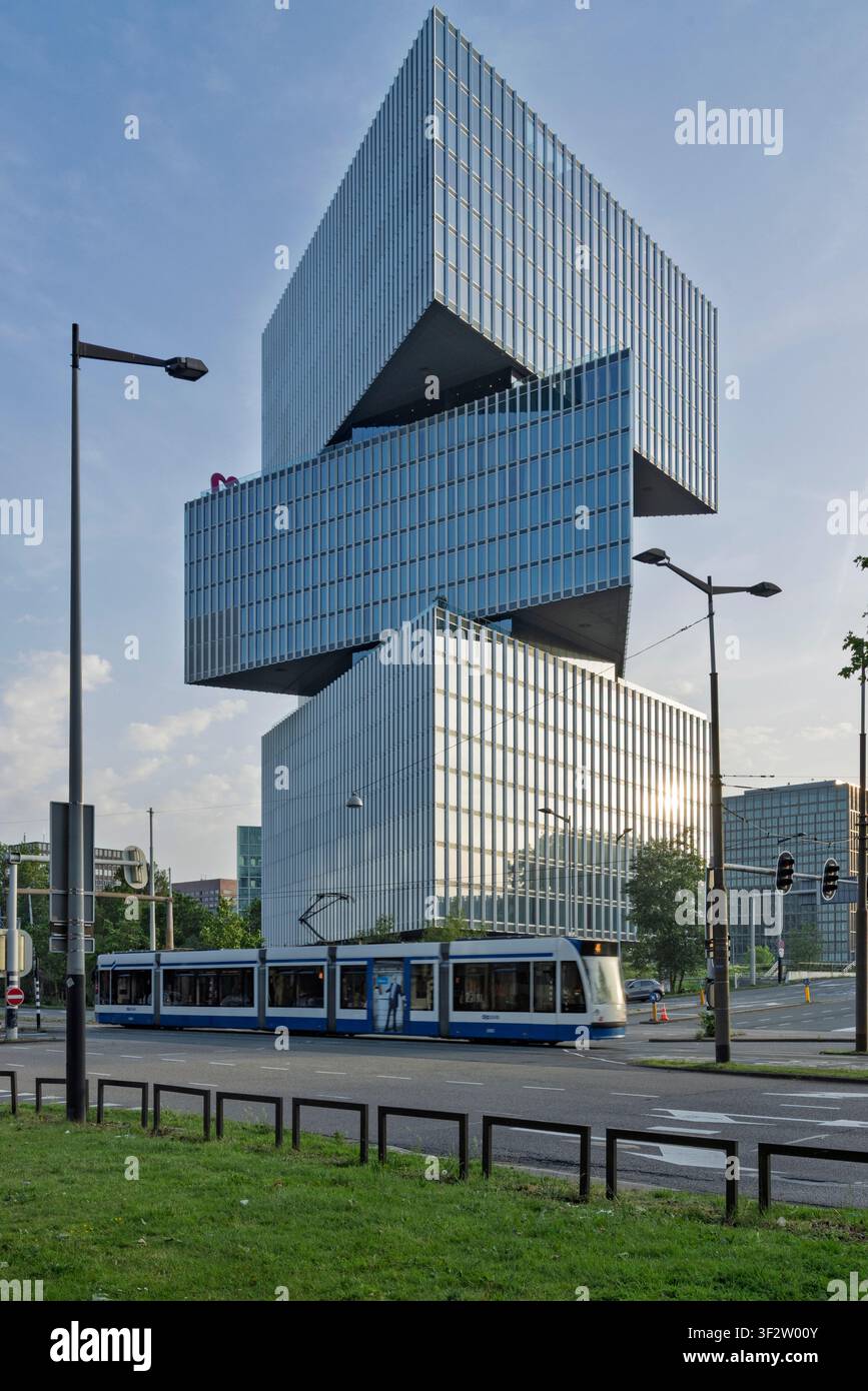 Amsterdam, Paesi Bassi, 23 maggio 2026. L'architettura futuristica in vetro dell'edificio dell'hotel nhow Amsterdam RAI con un tram pubblico blu e bianco Foto Stock