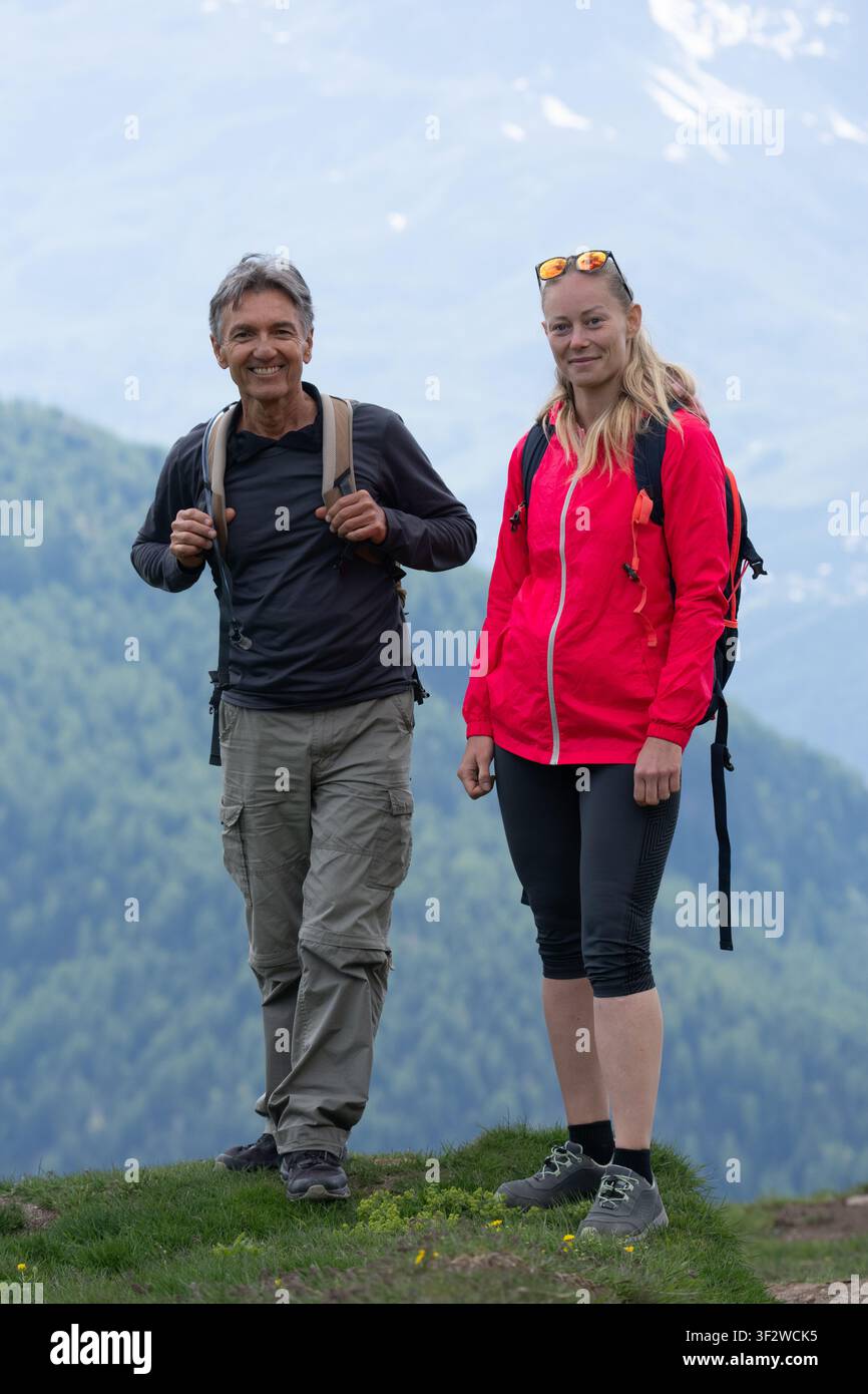 Coppia felice in piedi sulla cima della montagna con alberi verdi e cielo nuvoloso sullo sfondo Foto Stock