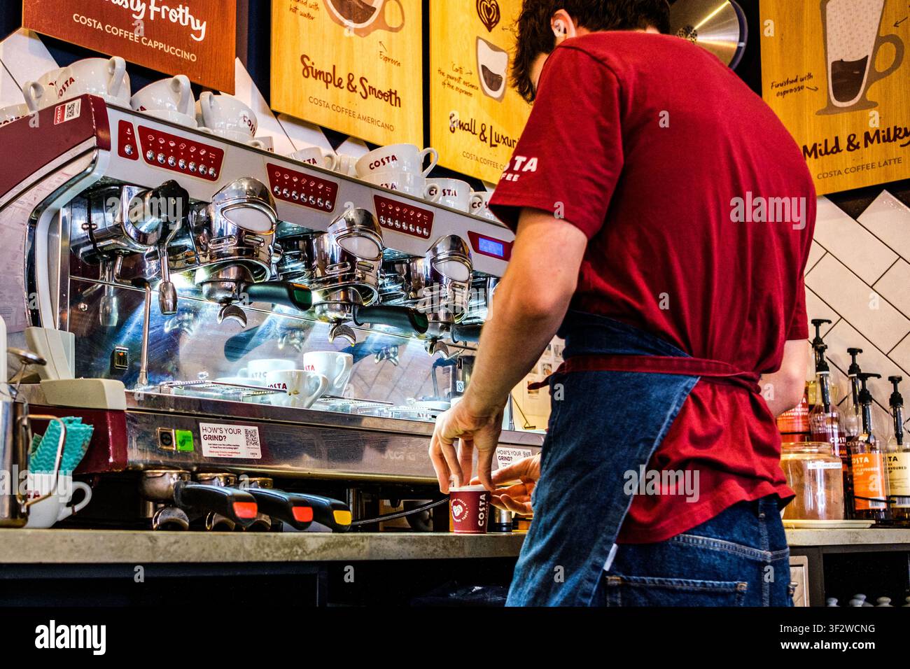 Leatherhead Surrey UK, 20 luglio 2026, Primo piano di un barista di spalle che prepara una bevanda calda al caffè per un cliente da Costa Foto Stock