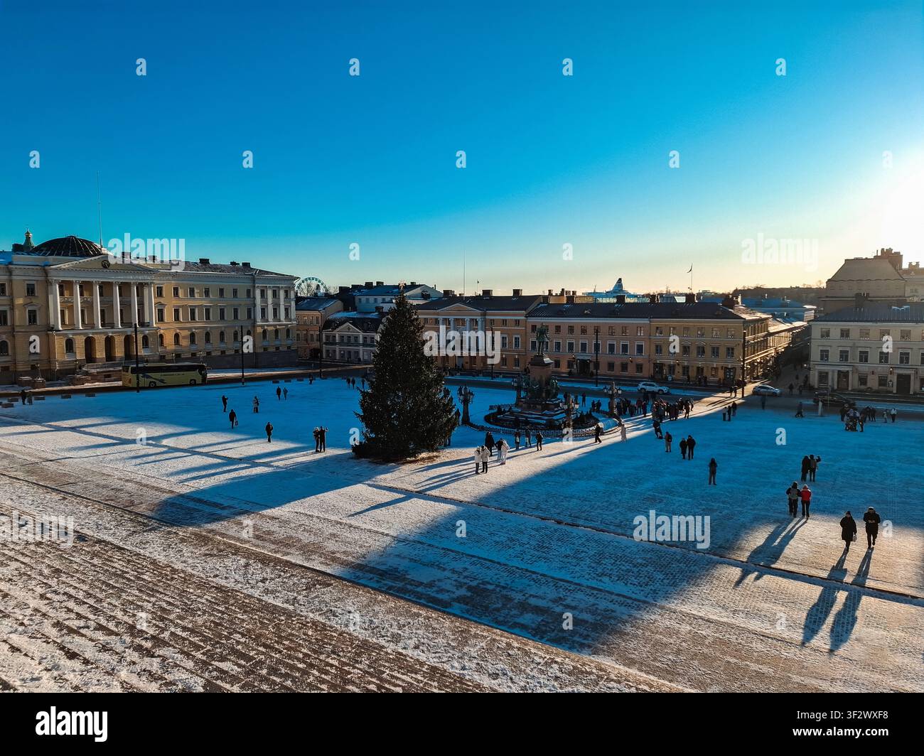 Helsinki, Finlandia - 31 dicembre 2025: Vista della piazza del Senato coperta di neve con un grande albero di Natale e persone che attraversano la piazza storica Foto Stock