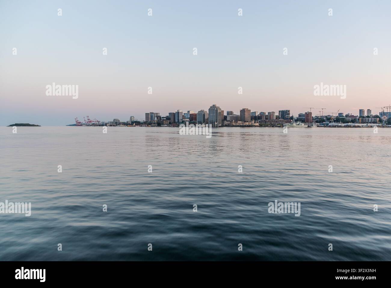 Lo skyline di Halifax, con i suoi grattacieli bagnati dalla luce serale, visto dalla parte di Dartmouth del porto, Canada. A sinistra dell'immagine ci sono le gru della Halifax Shipyard sulla riva nord della città. Dartmouth, Nuova Scozia, Canada Foto Stock
