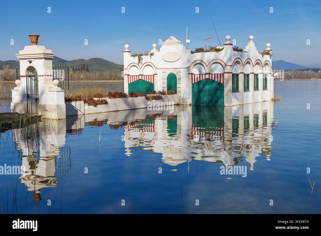 L'iconico Pesquera Marimon riflesso nelle acque tranquille del lago di Banyoles in un chiaro mezzogiorno in Catalogna, Spagna. La scena cattura il pacifico a Foto Stock
