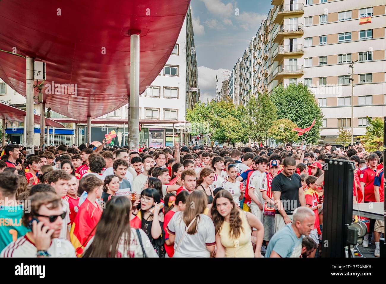 Grande folla di persone diverse radunate in una piazza cittadina, indossa maglie da calcio rosse e mostra entusiasmo mentre guarda una trasmissione di un importa Foto Stock