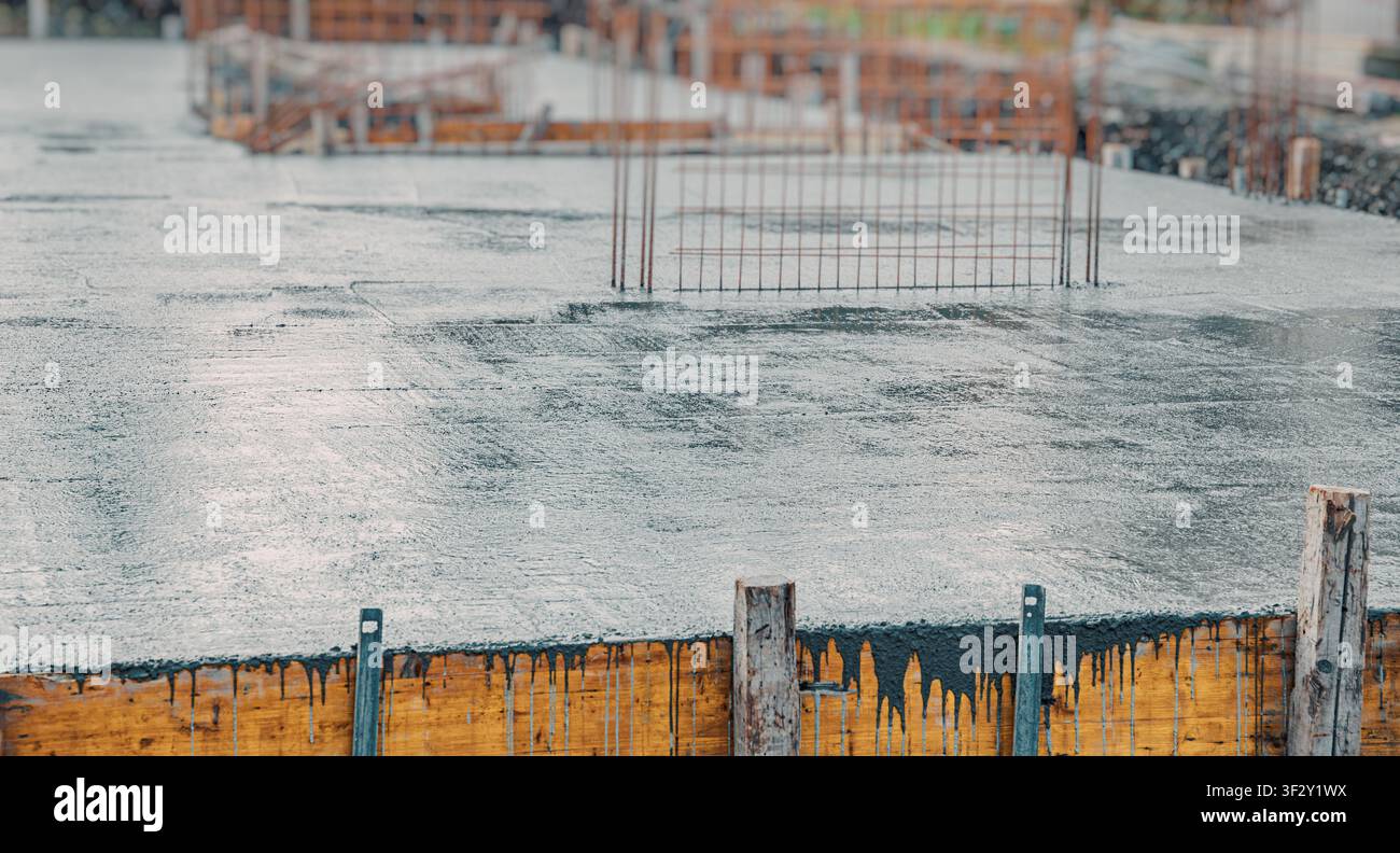 Piatto di fondazione in cemento bagnato con getto e rete di rinforzo in acciaio in un cantiere edile Foto Stock