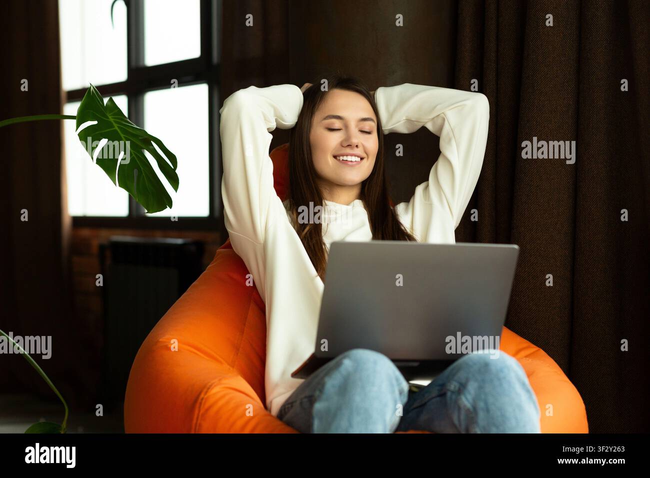 Sorridente bella donna sittingon su poltrona con computer portatile Foto Stock