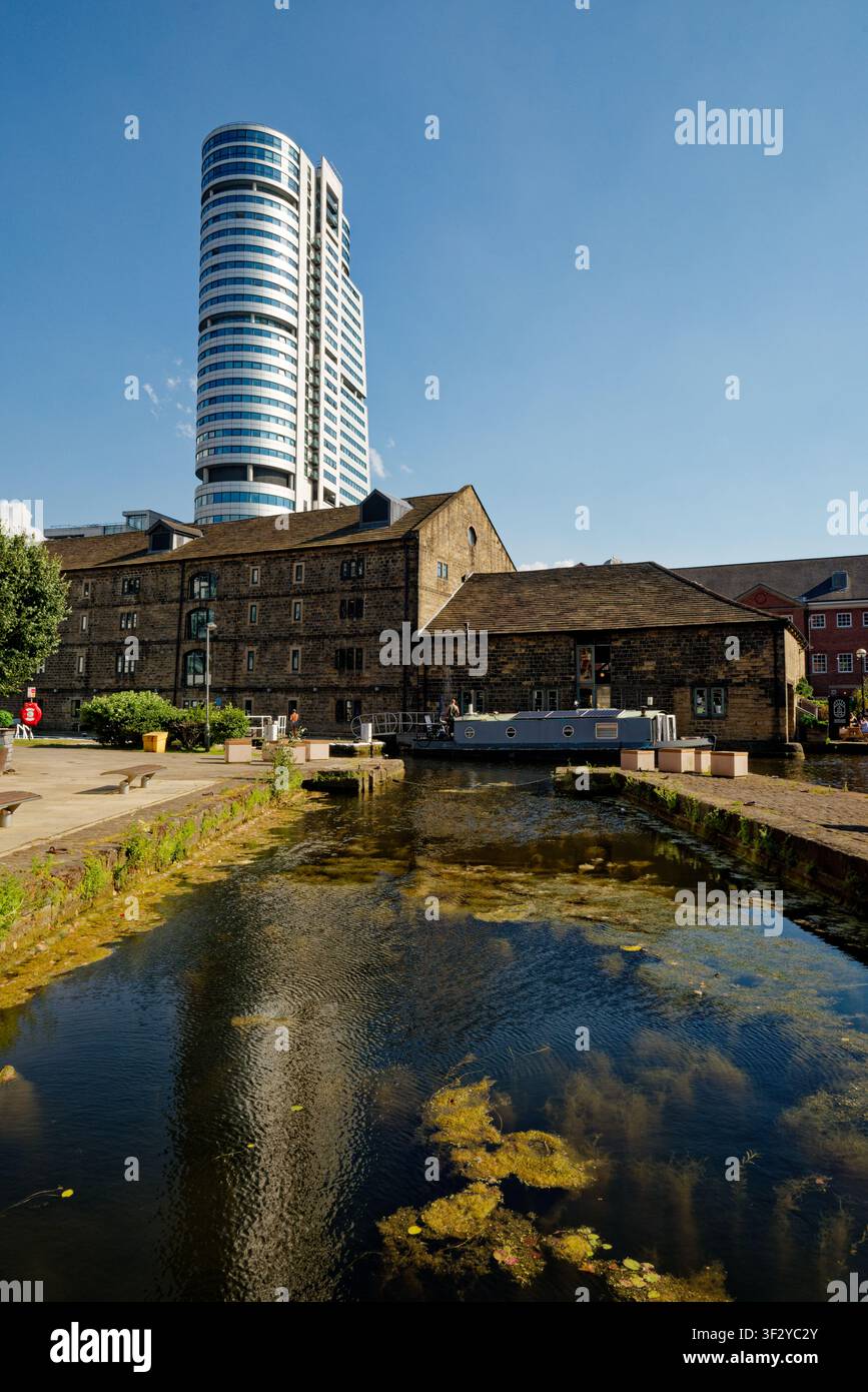 Un canale in un contesto urbano con vecchi magazzini e un alto edificio per uffici che si erge al di sopra, Granary Wharf, Leeds, West Yorkshire. Foto Stock