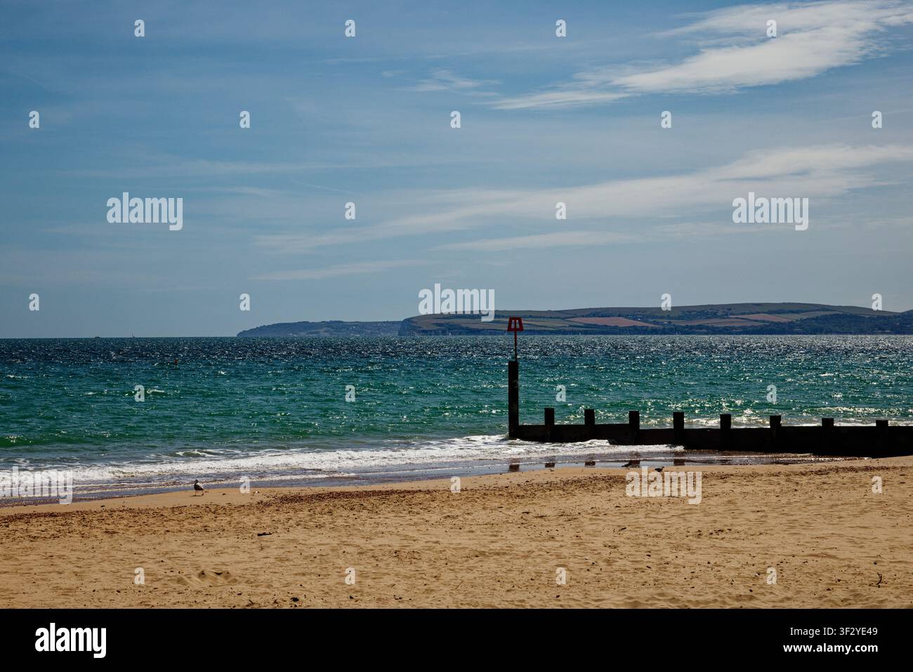 Morbide onde che lambiscono una spiaggia di sabbia dorata con una groyne e un promontorio lontano attraverso un mare blu-verde, Bournemouth, Dorset, Inghilterra. Foto Stock
