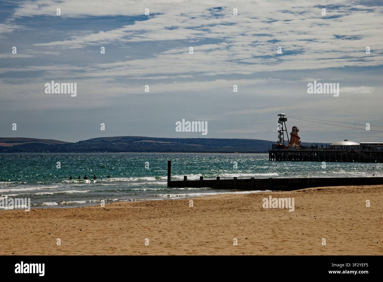 Un gruppo di persone che nuotano nel mare accanto a una groyne attraverso una spiaggia sabbiosa con un molo per il piacere sullo sfondo, Bournemouth, Dorset, Inghilterra. Foto Stock