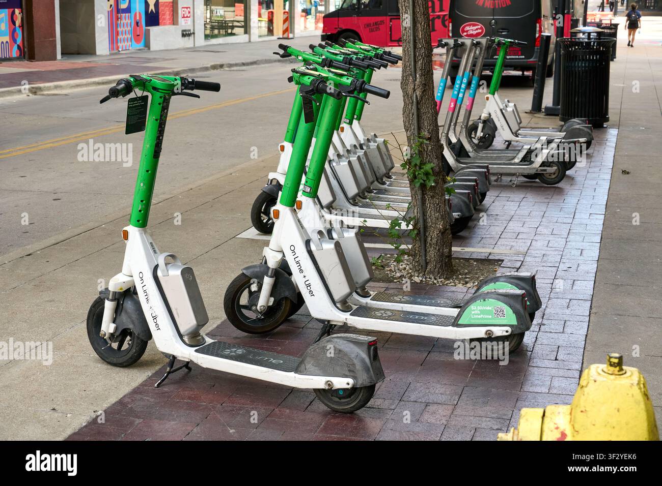 DALLAS, TX, USA - 11 LUGLIO 2026: Una fila di scooter elettrici Lime e Uber è ordinatamente allineata lungo un marciapiede a Dallas, Texas. Questi scooter sono par Foto Stock