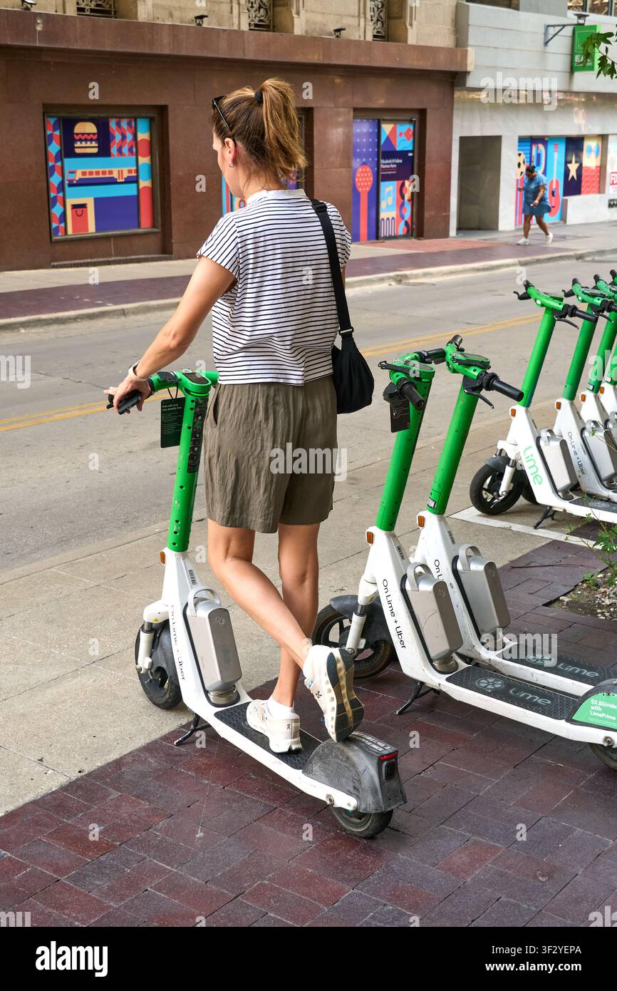 DALLAS, TX, USA - 11 LUGLIO 2026: Una persona è vista mentre interagisce con uno scooter Lime parcheggiato su un marciapiede in città. Gli scooter Lime sono veicoli elettrici popolari Foto Stock
