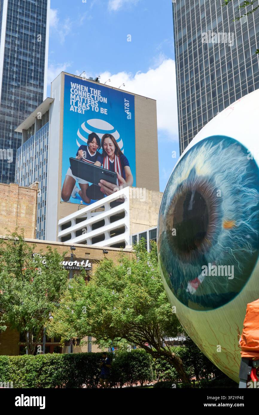 DALLAS, TX, USA - 11 LUGLIO 2026: Una grande scultura oculare e una pubblicità ATandT sono esposte in modo prominente nel centro di Dallas. L'arte urbana surreale Foto Stock