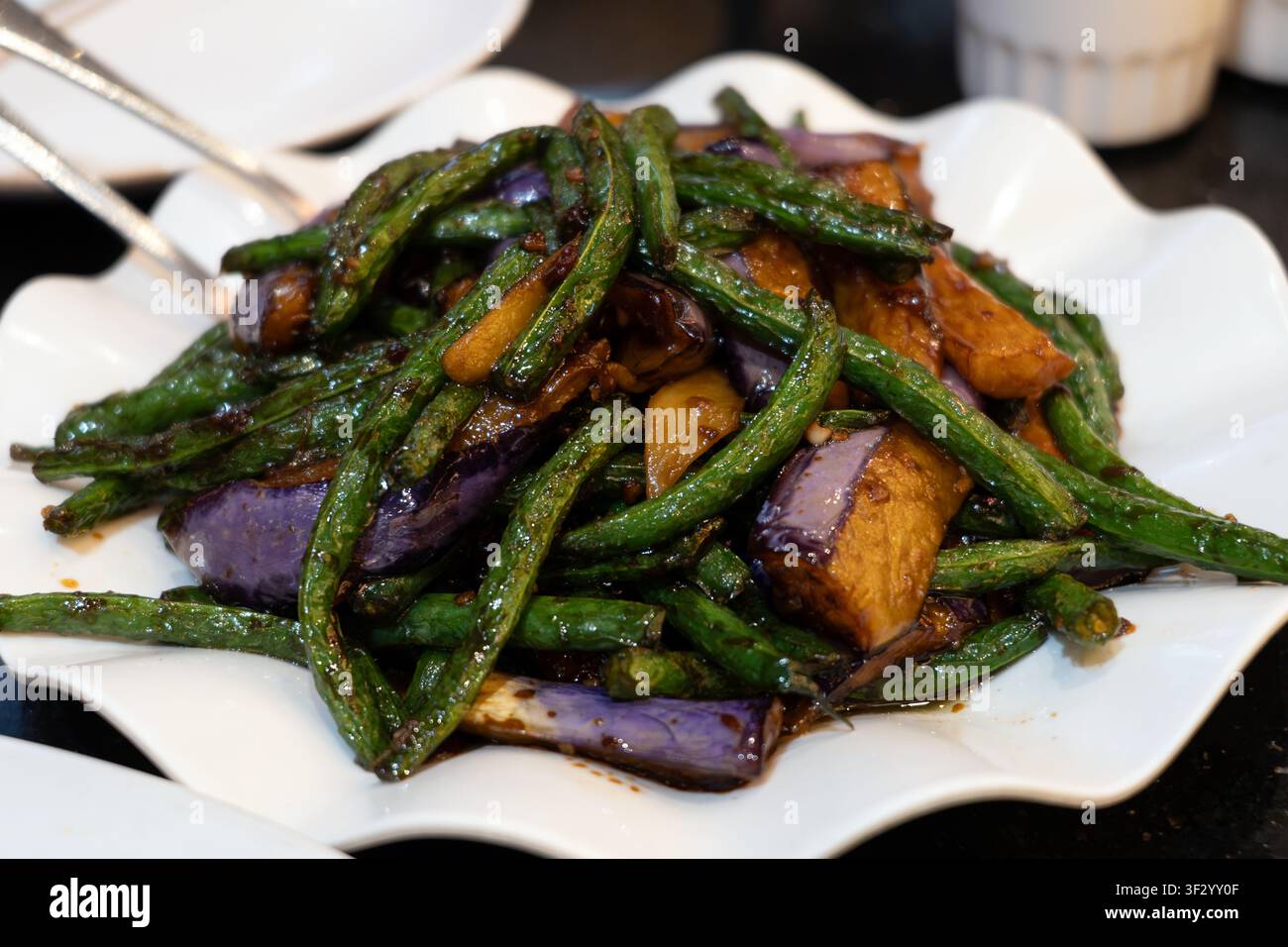 Fagioli lunghi cinesi saltati e melanzane conditi con una salsa di soia all’aglio saporita. Questo piatto vegetale presenta colori vivaci, una consistenza tenera-crudente e ricche note umami. Foto Stock