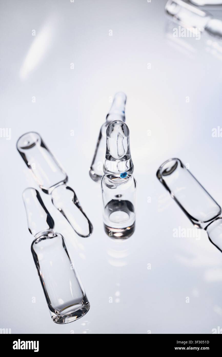 Ampolle di vetro sterili su superficie riflettente, simboleggianti ricerca e assistenza sanitaria Foto Stock
