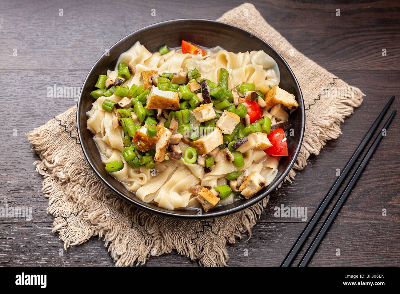 Nudli piatti fatti a mano saltati con tofu a cubetti, fagiolini, funghi e pomodori freschi Foto Stock