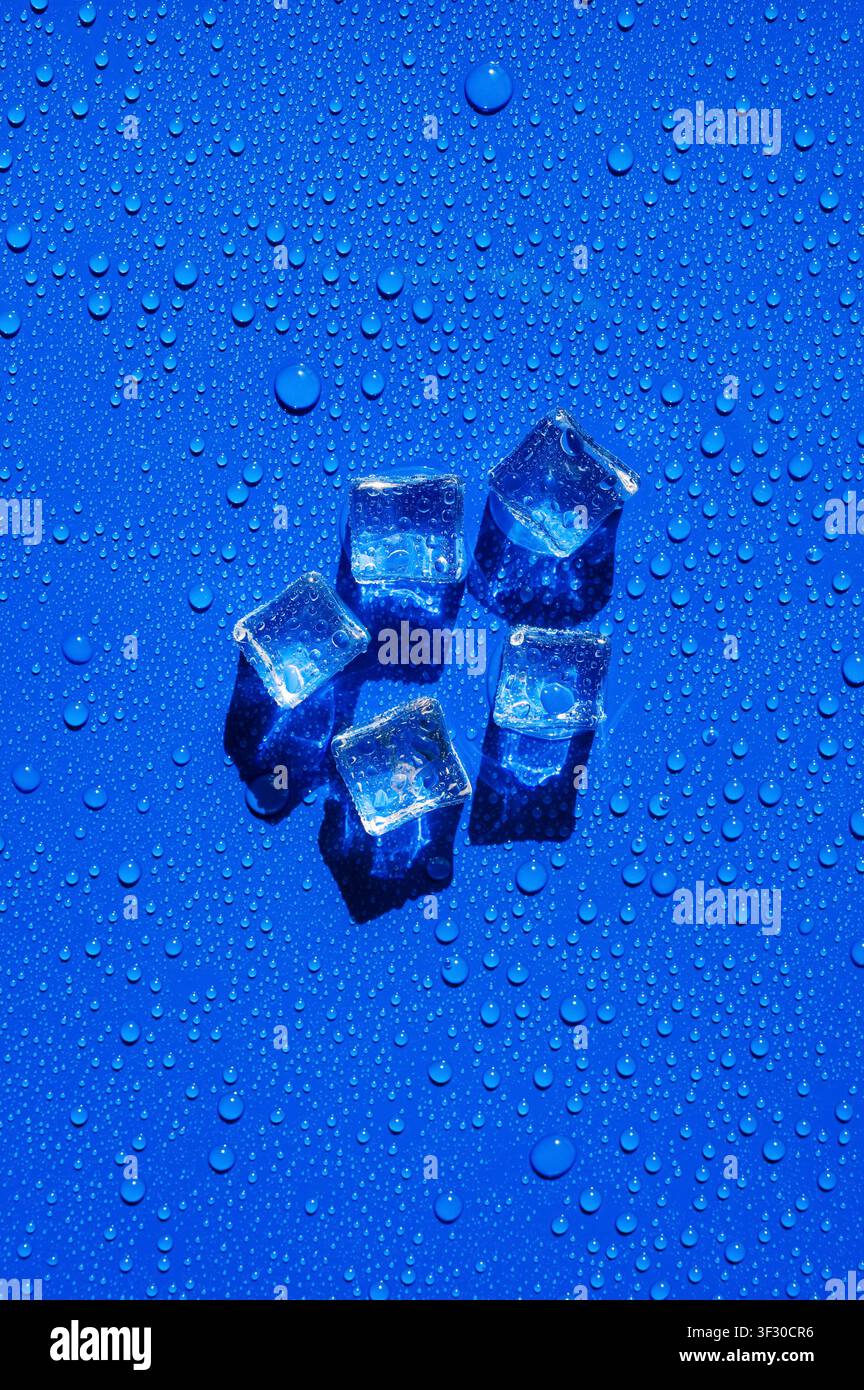 Ghiaccioli trasparenti disposti su una superficie blu vivace e bagnata con gocce d'acqua. Foto Stock