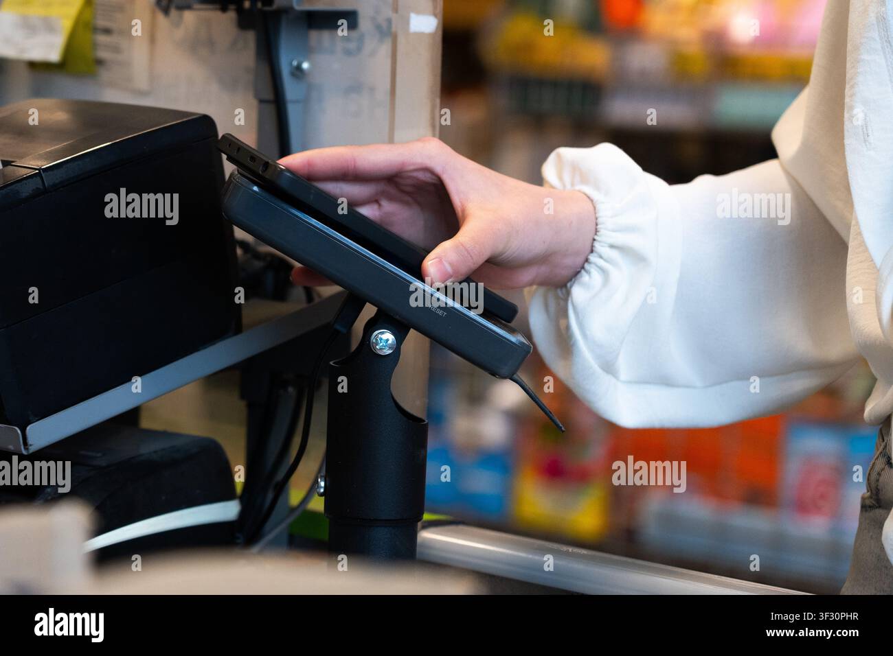 Mano che tiene un dispositivo mobile per un pagamento contactless a un sistema di punto vendita in un ambiente di vendita al dettaglio Foto Stock