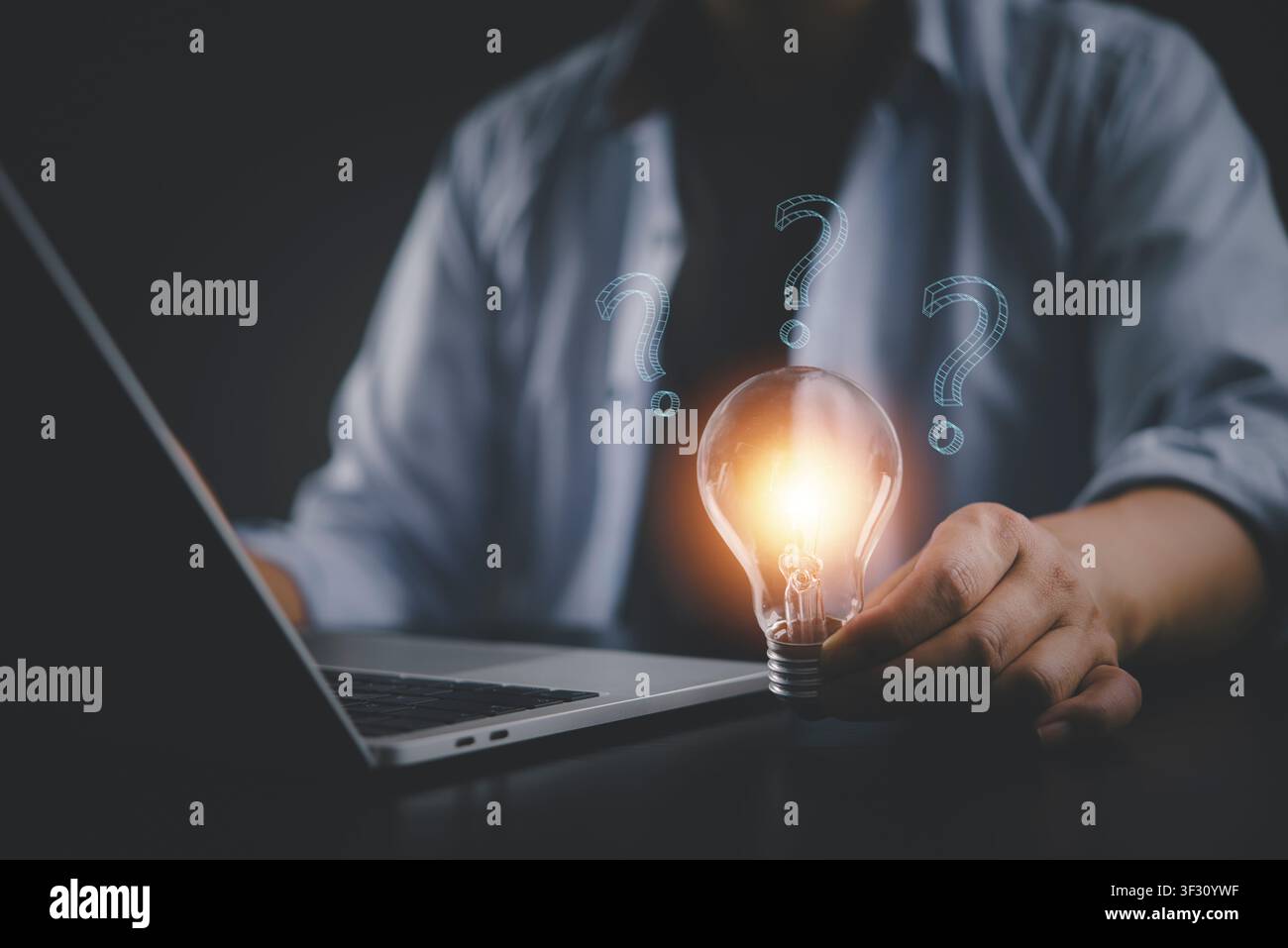 Uomo d'affari che tiene una lampadina luminosa con punti interrogativi digitali sulla scrivania del laptop. Concetto di risoluzione dei problemi, soluzione aziendale innovativa, creativa t Foto Stock