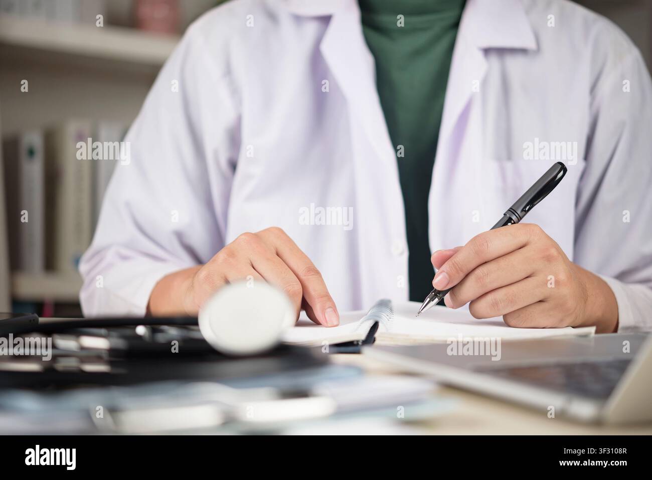 Medico o studente di medicina che scrive appunti in un quaderno con stetoscopio e laptop sulla scrivania. Concetto di istruzione medica, ricerca clinica, un Foto Stock