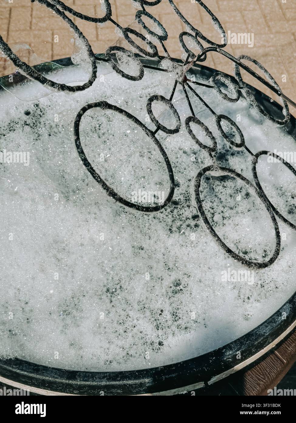 Primo piano di più bastoncini per bolle di sapone appoggiati in una bacinella di acqua saponata coperta da una schiuma abbondante. Un'immagine giocosa e strutturata ideale per l'infanzia, l'attività all'aperto Foto Stock