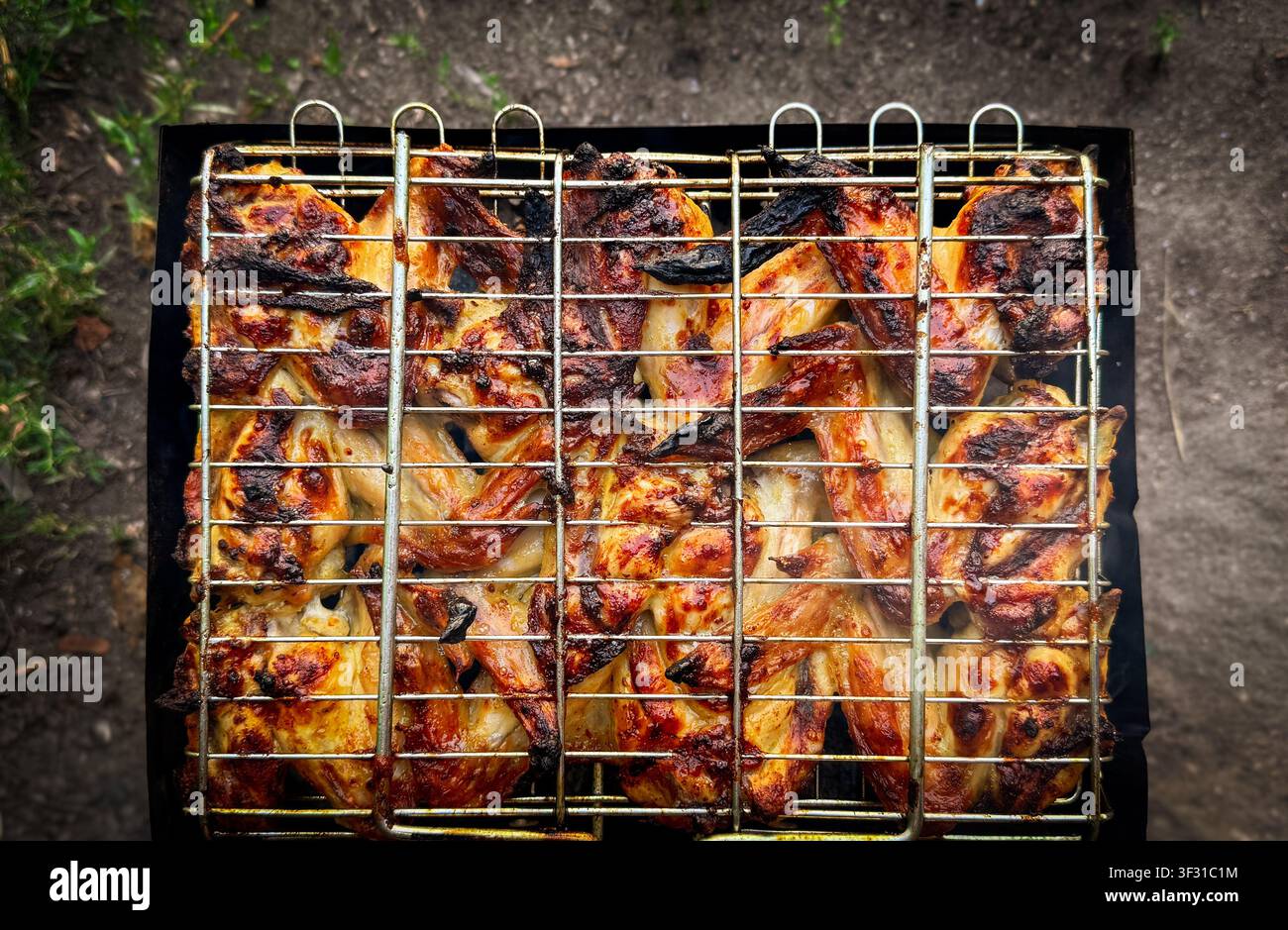 Vista ravvicinata dall'alto di ali di pollo marinate che cuociono in un cestino grigliato di filo metallico sopra un fuoco aperto. Foto Stock