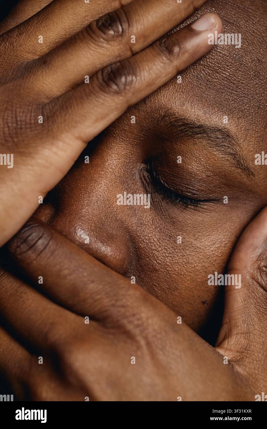Uomo nero che copre il viso esprimendo stress e stanchezza mentale Foto Stock