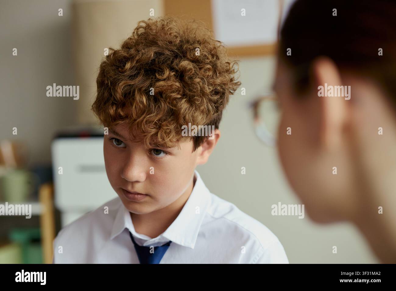 Ragazzino caucasico che ascolta durante una sessione di consulenza con un'insegnante, mostrando preoccupazione e sostegno emotivo in classe. Utile per temi legati all'educazione, al benessere dei bambini e alla guida Foto Stock